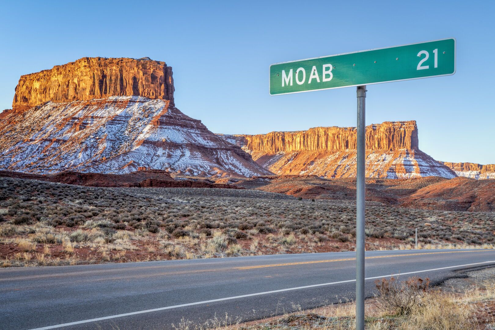 Señal de carretera para 'MOAB 21', con vista despejada a un paisaje desértico y formaciones rocosas.