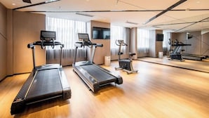 Una palestra moderna in hotel con tre tapis roulant, una cyclette e una parete con specchi.