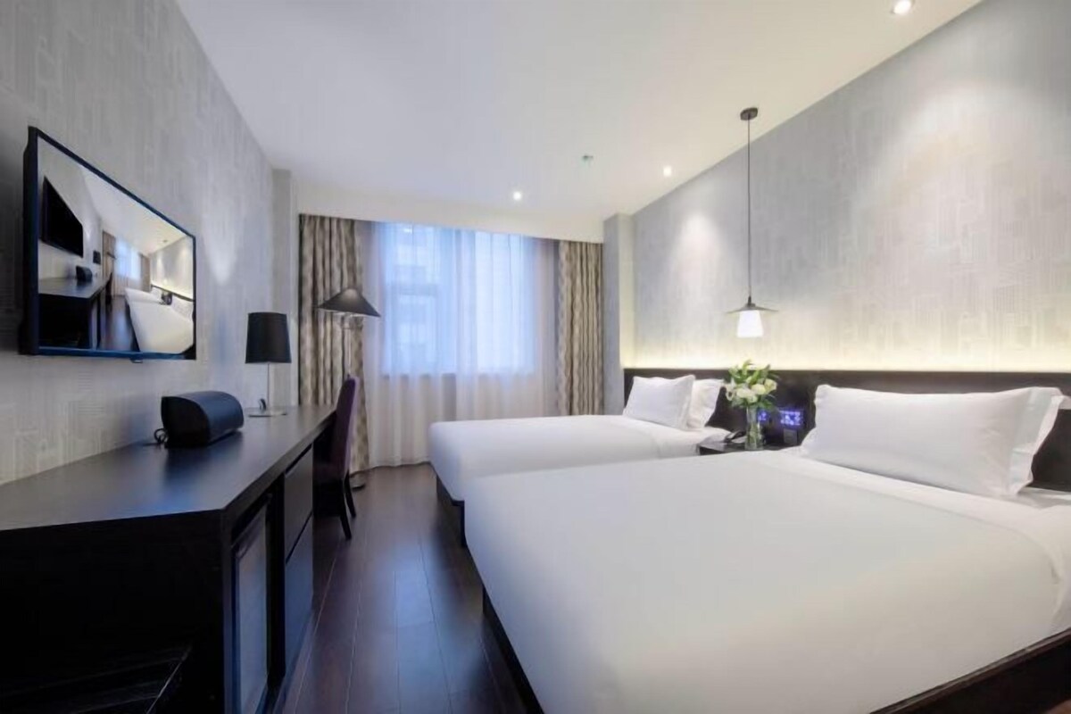 A hotel room with two beds, a desk, a chair, a lamp, and a large mirror.