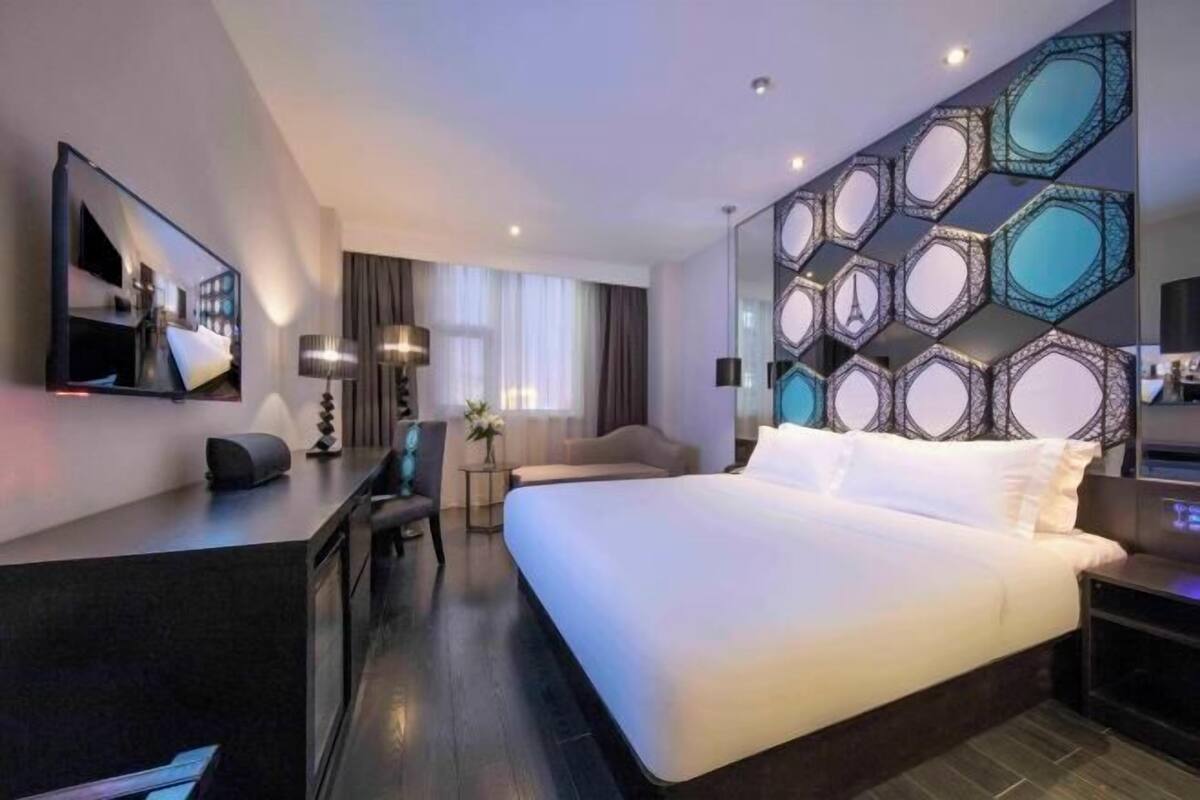 Habitació d'hotel moderna amb un llit gran, escriptori, cadira, televisió i un panell decoratiu a la paret.