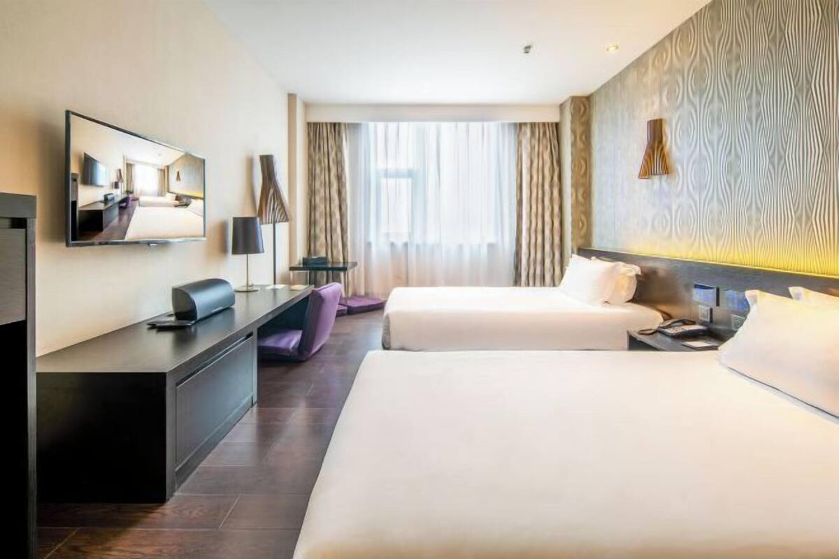 Habitació d'hotel amb dos llits, una taula de treball, televisió i una finestra gran amb cortines.