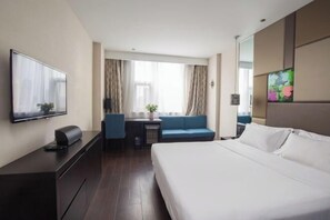 A modern hotel room with a large bed, a flat-screen TV mounted on the wall, a desk with a chair, and a sofa. - Orange Hotel (Hefei Sanxiaokou Subway Station Store) (Hefei)