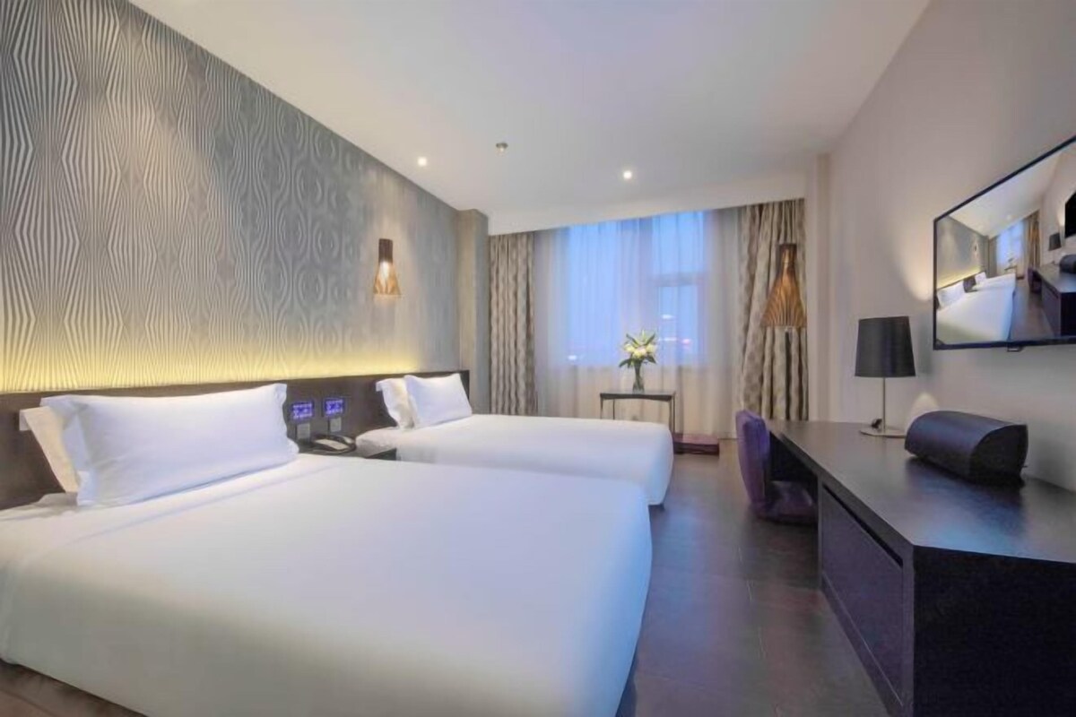 A hotel room with two beds, a desk, a chair, a lamp, and a large mirror.