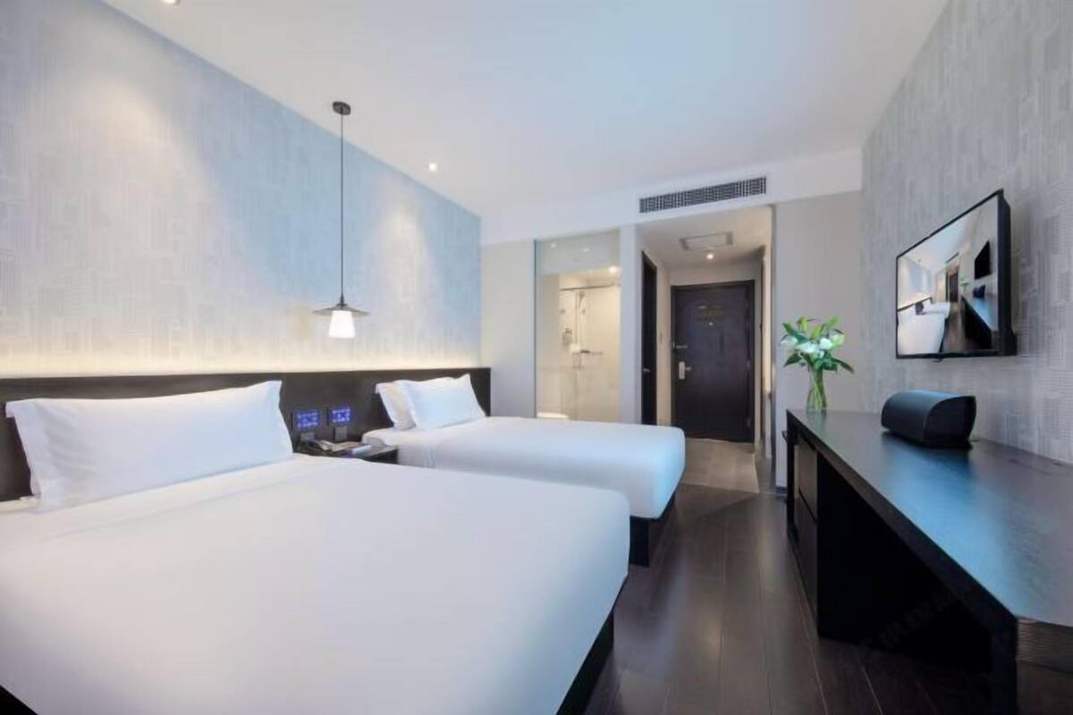 Habitació d'hotel amb dos llits, escriptori, televisió i bany visible a través d'una porta oberta.