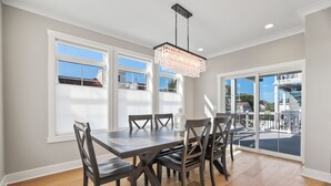 Un comedor con una mesa grande, varias sillas, una araña y ventanas amplias que ofrecen vistas al exterior.