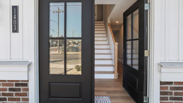 Una puerta negra con un panel de vidrio, un muro de ladrillo y una escalera de madera que da al interior.