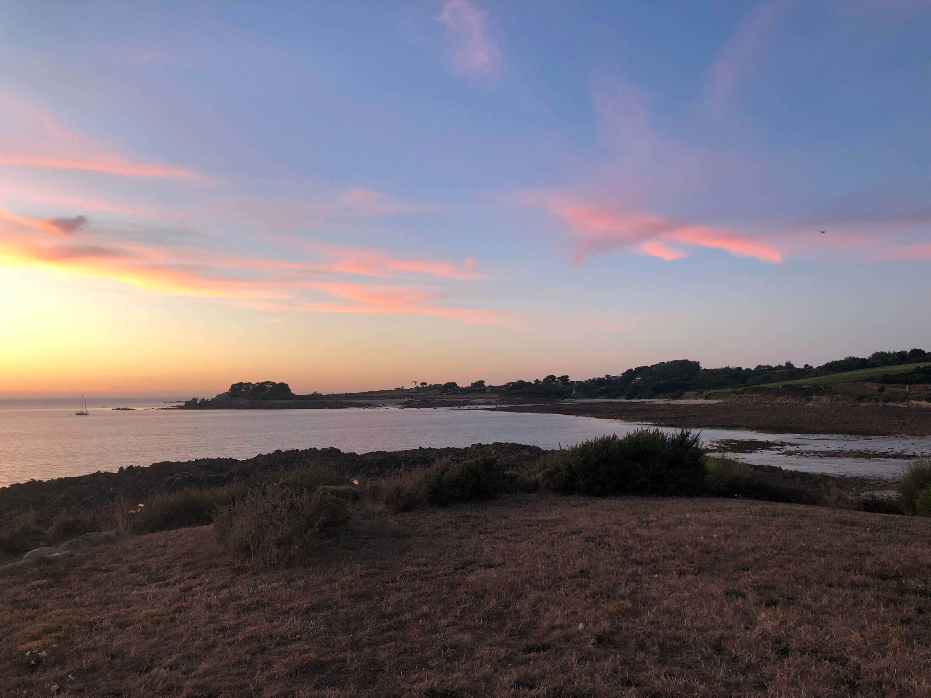 Een kustlandschap met een zonsondergang, grasvelden en een verre kustlijn.