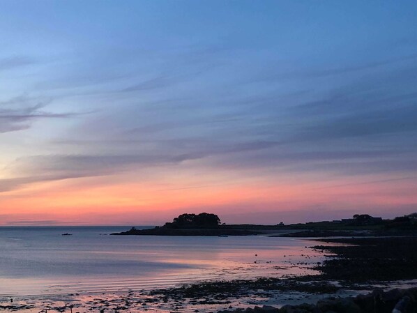 A coastal landscape with a sunset, calm sea, and a distant rocky outcrop.