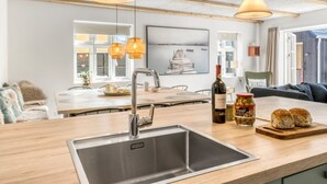 A modern kitchen with a stainless steel sink, wooden countertops, hanging pendant lights, and a dining area with a view of the sea.