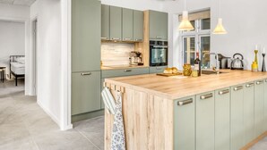 A modern kitchen with green cabinets, a wooden island, and pendant lighting.