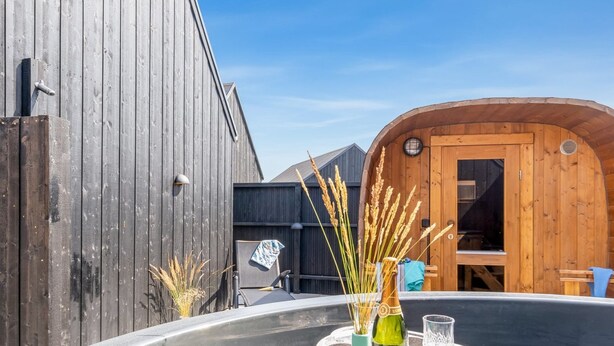 A hot tub with a stone pedestal, surrounded by wooden cabins and a wooden fence.