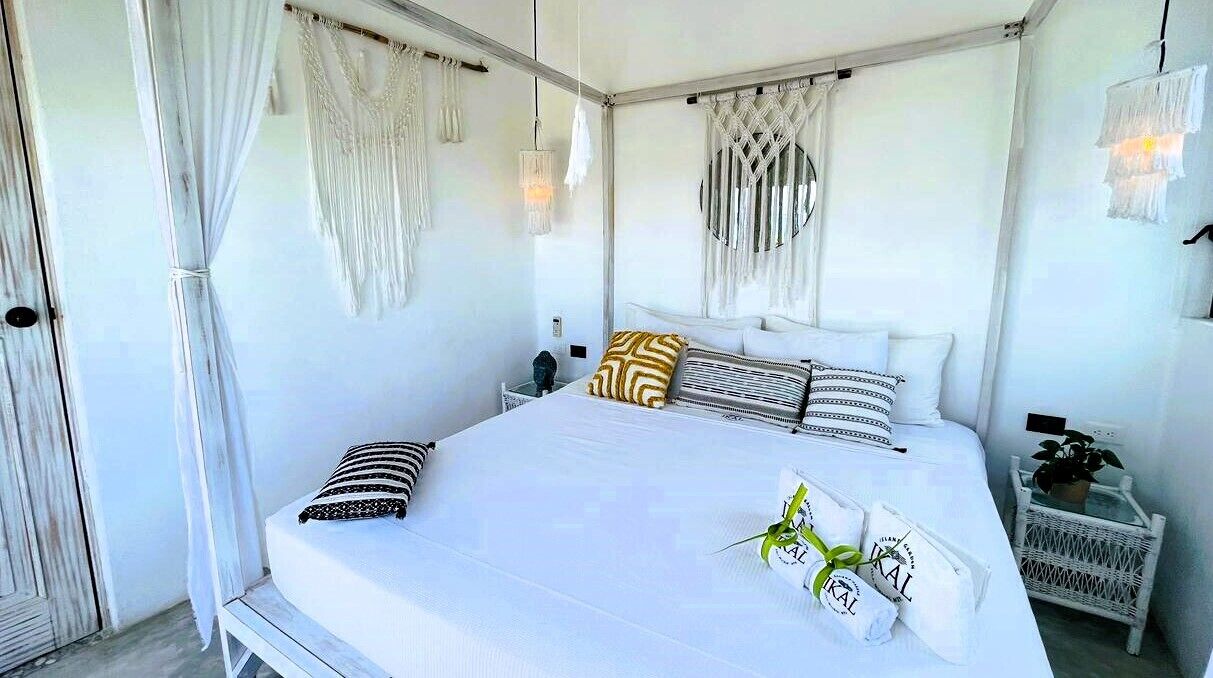 Un dormitorio con una cama grande, ropa de cama blanca y una mesita de noche con una planta.