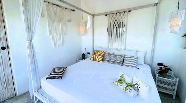 Un dormitorio con una cama grande, ropa de cama blanca y una mesita de noche con una planta.