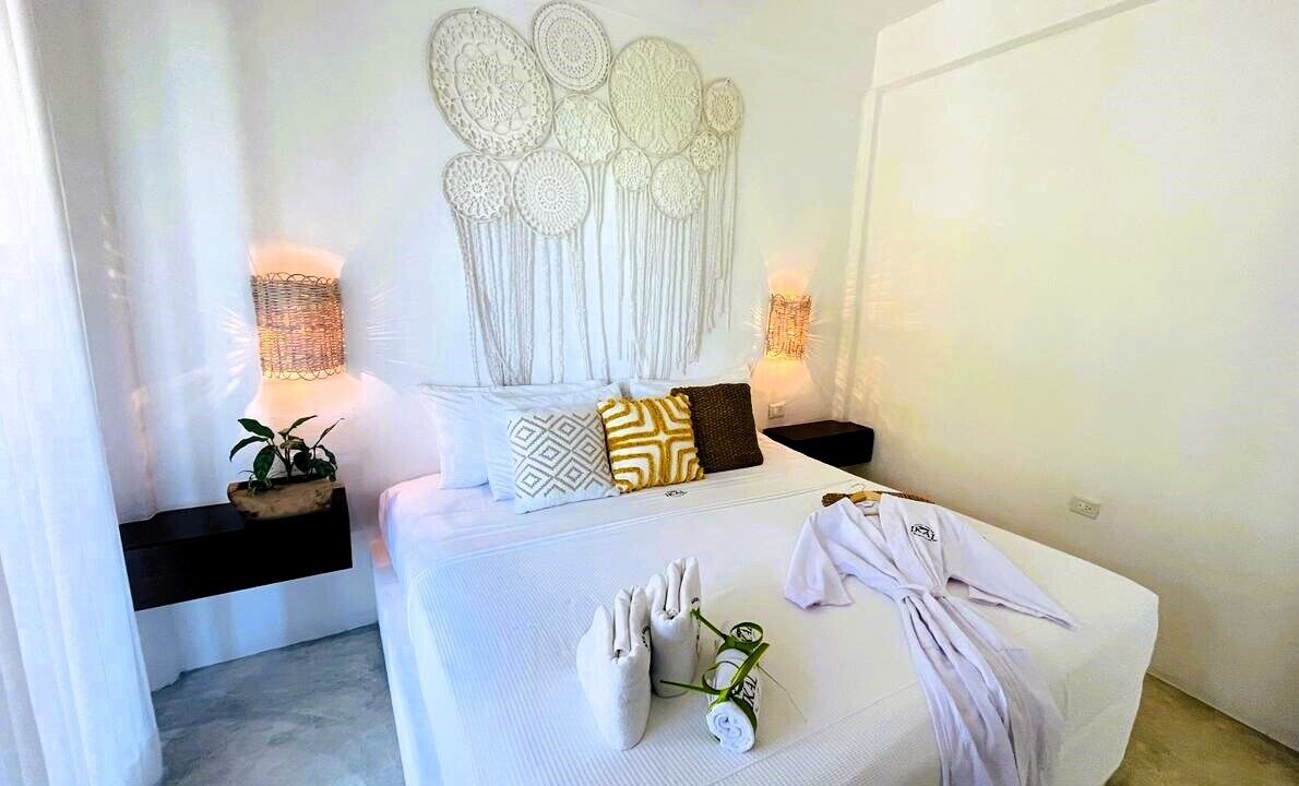 A modern bedroom with a large bed, decorative wall art, bedside lamps, and a potted plant.