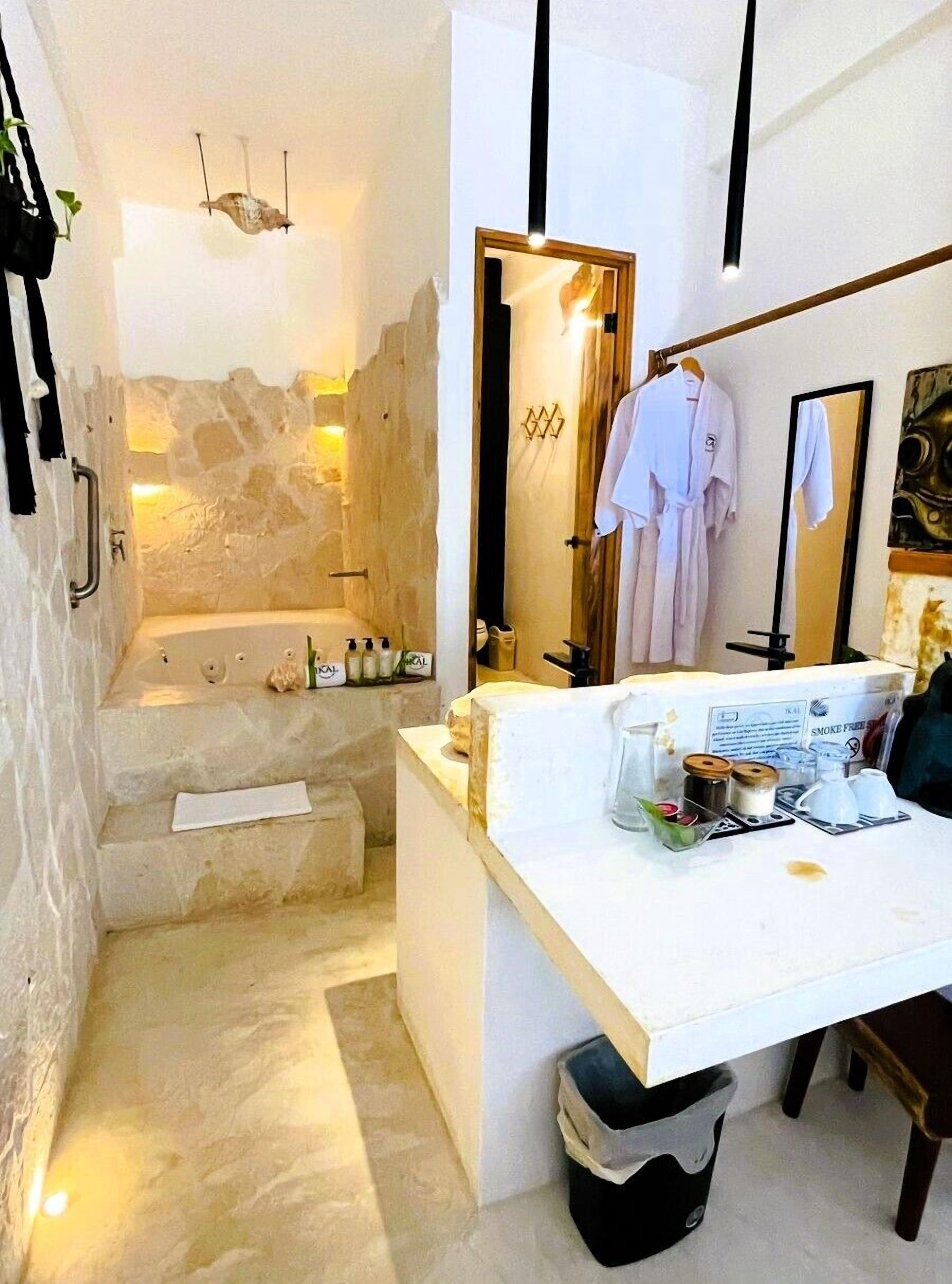 Un baño con bañera, lavamanos con artículos de aseo y una bata colgada en un perchero.