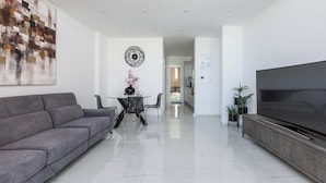 Una sala de estar moderna con un sofá gris, una mesa de comedor con sillas, un televisor sobre un mueble de madera y un cuadro abstracto grande en la pared.