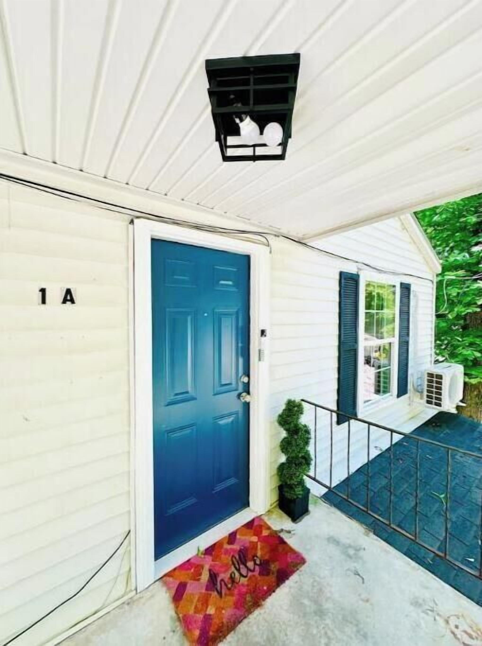 Une maison blanche avec une porte bleue, une lanterne noire au-dessus de la porte et un paillasson sur lequel est écrit « bonjour » à l’entrée.