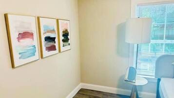 A bedroom with a bed, a bedside table, a lamp, and three abstract paintings on the wall.