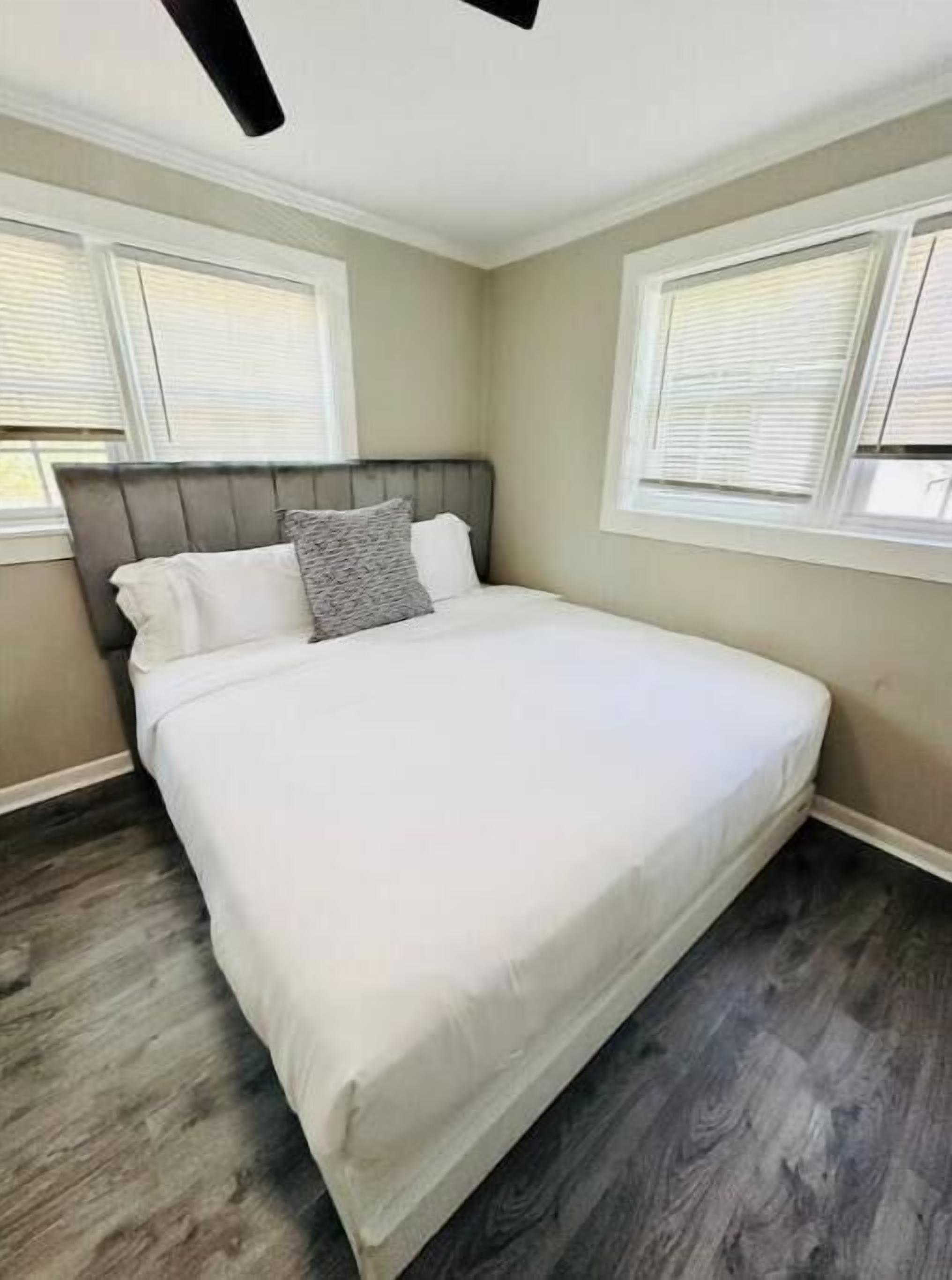 Quarto com cama, duas janelas com persianas e ventoinha no teto.