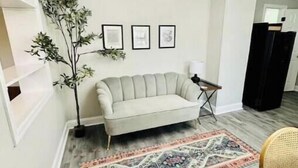 A living room with a light-colored sofa, a patterned rug, a tall plant, and a chandelier.
