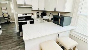 A modern kitchen with white cabinets, a central island with stools, a built-in oven, and a microwave.