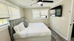 A bedroom with a bed, a ceiling fan, a TV mounted on the wall, and a window with blinds.