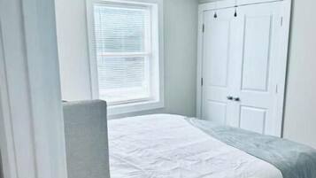 Ein Schlafzimmer mit einem Bett, einem Deckenventilator, einem Fenster mit Jalousien und einer Tür.