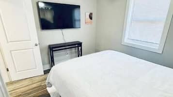 A bedroom with a bed, a ceiling fan, a TV mounted on the wall, and a window with blinds.