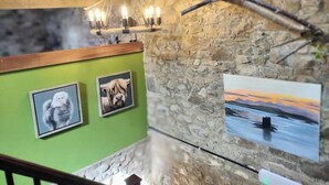 A room with a stone wall, a wooden ceiling, and a green wall with three framed pictures. - The Hayloft Rustic Glamping Barn, Caldbeck Village (Caldbeck)