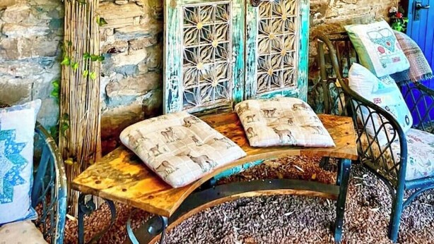 A rustic stone wall with a wooden bench and cushions, a blue door, and a switchboard with lights. - The Hayloft Rustic Glamping Barn, Caldbeck Village (Caldbeck)