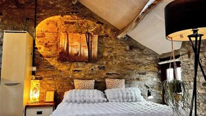 A bedroom with a stone wall, a bed with white bedding, a nightstand, a lamp, and a window. - The Hayloft Rustic Glamping Barn, Caldbeck Village (Caldbeck)