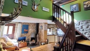 A cozy interior with a stone fireplace, a wooden staircase, and a green wall adorned with animal horns and pictures. - The Hayloft Rustic Glamping Barn, Caldbeck Village (Caldbeck)