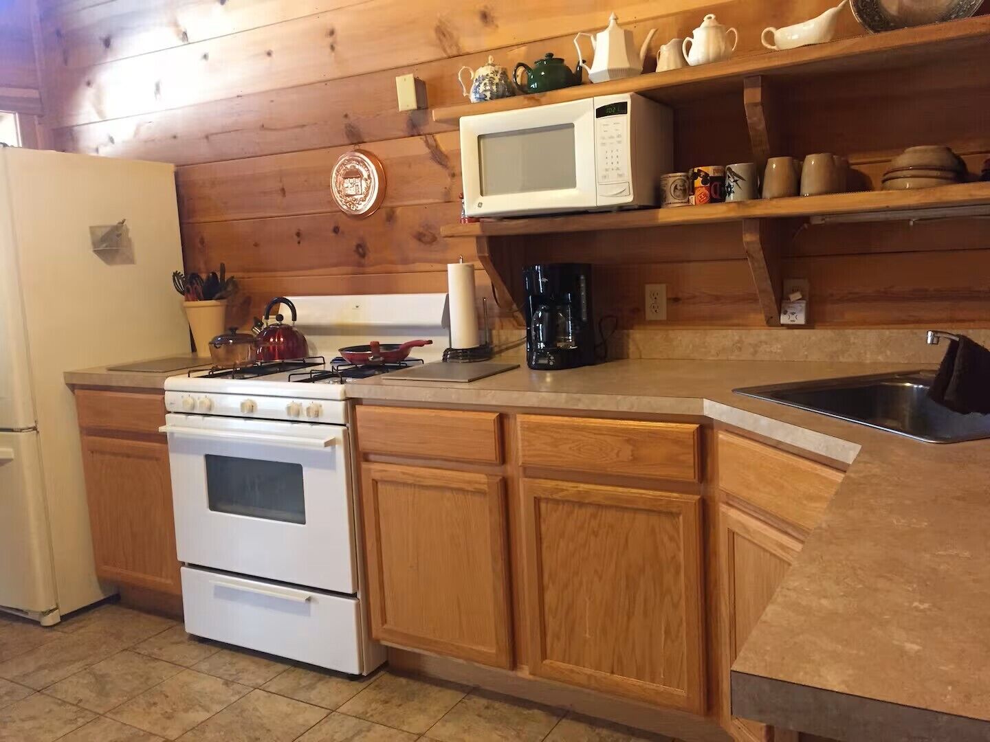 Una cocina con armarios de madera, estufa, microondas y cafetera.