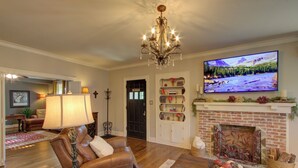 Una sala de estar con chimenea, televisor, sillones de cuero y una araña.
