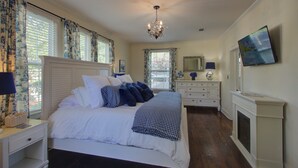 Une chambre à coucher avec un grand lit, une commode, un miroir, une télévision et une cheminée.