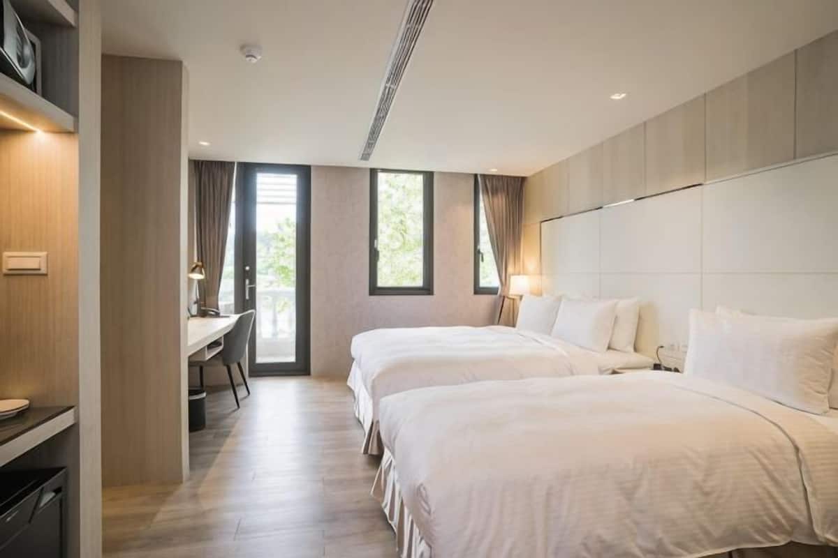 Ein modernes Hotelzimmer mit zwei Betten, einem Schreibtisch und Blick ins Freie.