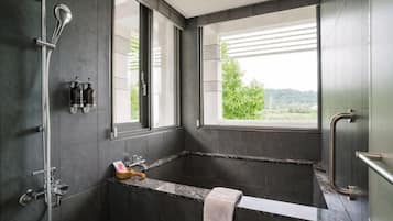 Uma casa de banho moderna com uma banheira grande, chuveiro e janela com vista para o verde.