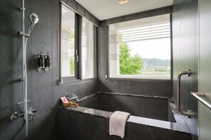 A modern bathroom with a large bathtub, a shower, and a window providing a view of greenery. - Inn Rose (Taoyuan)