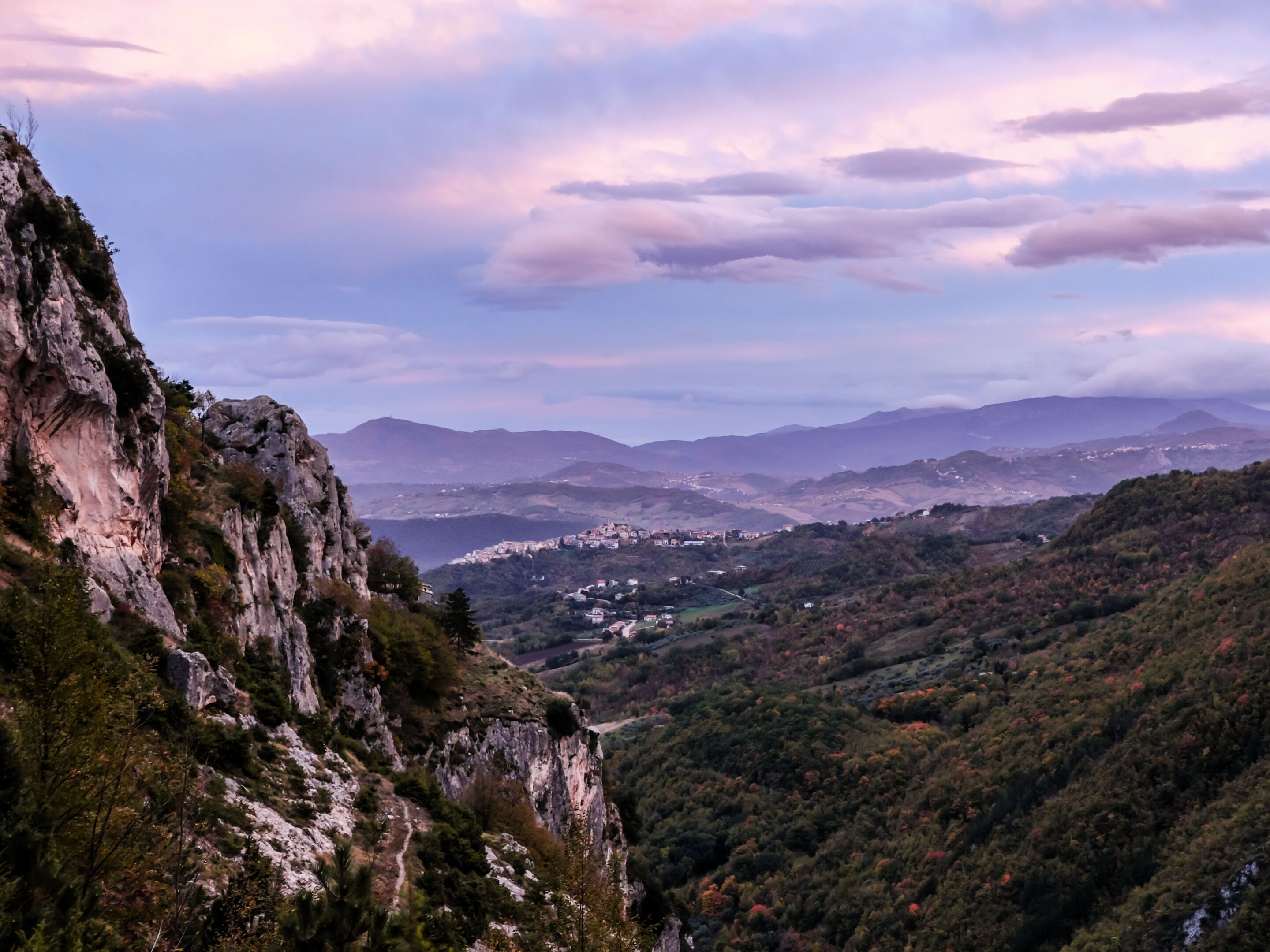 A mountainous landscape with rocky cliffs and a valley with scattered buildings.