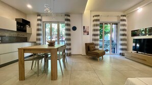 Una sala de estar moderna con una mesa de comedor de madera, un sofá, un televisor y una cocina con mostrador y armarios.