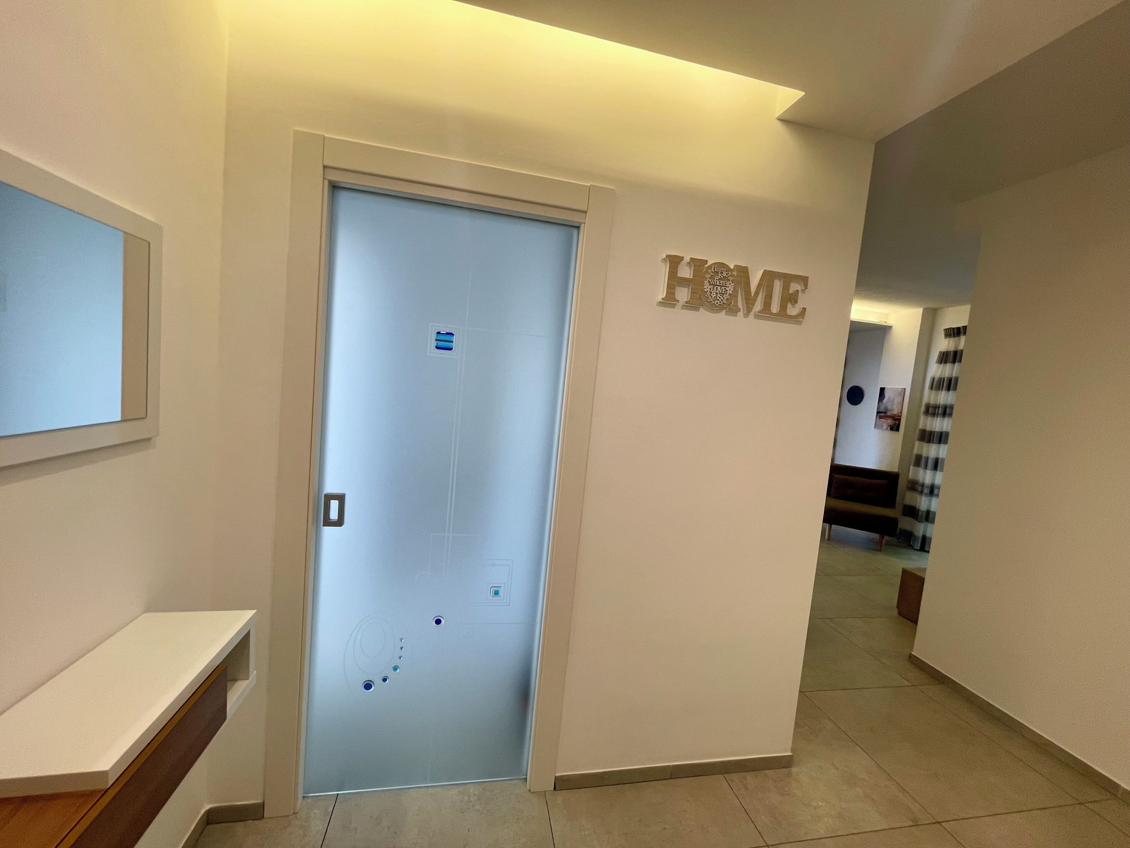 Ein Flur mit einer Tür, auf der „HOME“ steht, einem kleinen Regal und einem an der Wand befestigten Schild.