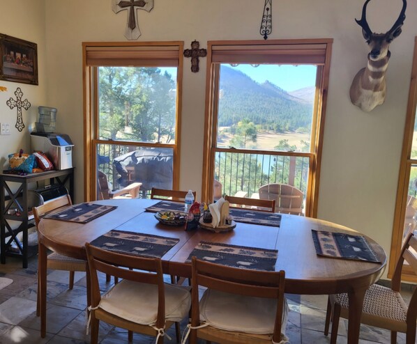 A dining area with a round table, chairs, and a view of a mountainous landscape through large windows.