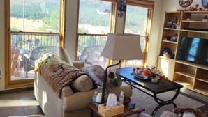 A cozy living room with a sofa, a table with a lamp, and a TV. Large windows offer a view of the outdoors. - Charming country house with WiFi in Nutrioso (Nutrioso)