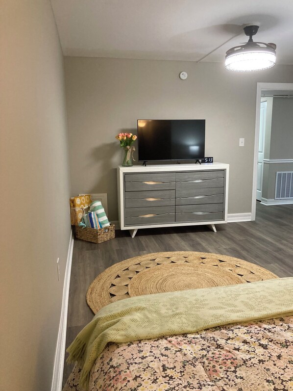 Un dormitorio con cama, cómoda, televisor y ventilador de techo.