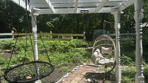 Un jardín con un pérgola, una silla colgante y una jaula de pájaros.