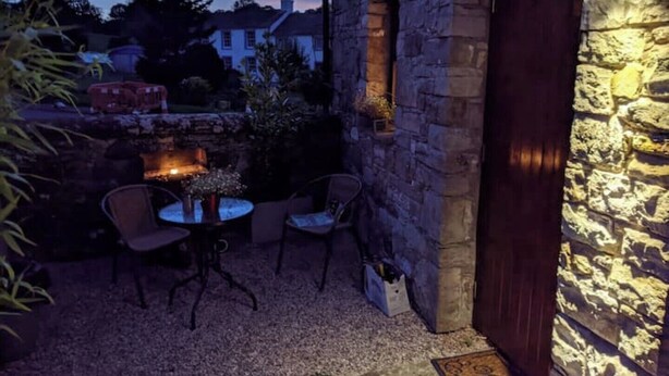 An outdoor seating area with stone walls, a fire feature, and a small table with chairs. - Glamping Barns & Bothy, in Caldbeck, Lake District (Caldbeck)