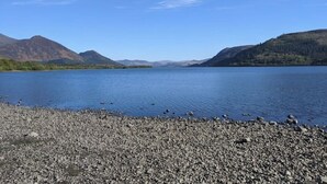 A lake with a rocky shoreline and distant mountains under a clear sky. - Glamping Barns & Bothy, in Caldbeck, Lake District (Caldbeck)