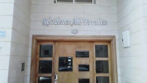 Ein Gebäudeeingang mit einem Schild, auf dem 'Residence Ahl Errahim' steht, und einer zweiflügeligen Holztür mit mehreren Fenstern.