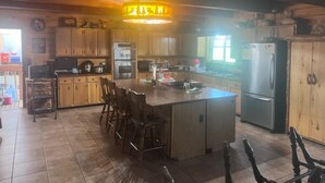 Une cuisine spacieuse avec des meubles en bois, un îlot central doté de tabourets et un grand lustre.