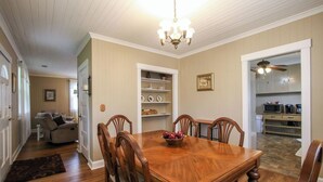 A dining room with a wooden table and chairs, a chandelier, and a kitchen visible through an open doorway. - Miss Audrey’s House is a charming cottage in the heart of historic Richmond Hill (Richmond Hill)